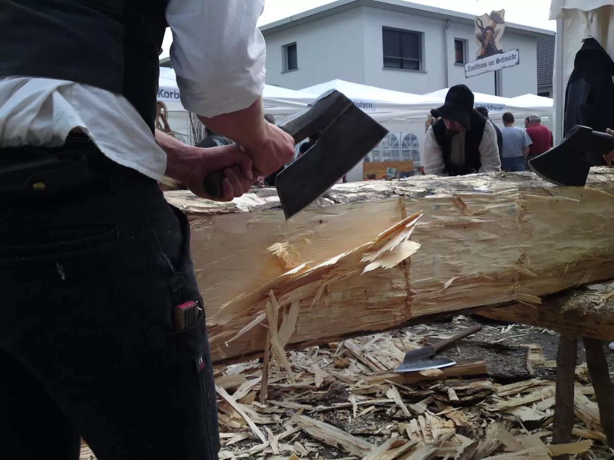 Zimmermann schintet bereits blanken liegenden Baumstamm mit einem alten Beil