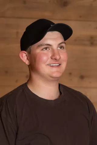 Mitarbeiterportrait / Foto mit braunem T-Shirt oder schwarzem Polo Shirt mit Zimmerei Hirschi Logo. Strahlend und lachend nach oben schauend oder direkt in die Kamera.