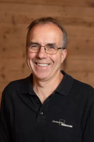 Mitarbeiterportrait / Foto mit braunem T-Shirt oder schwarzem Polo Shirt mit Zimmerei Hirschi Logo. Strahlend und lachend nach oben schauend oder direkt in die Kamera.